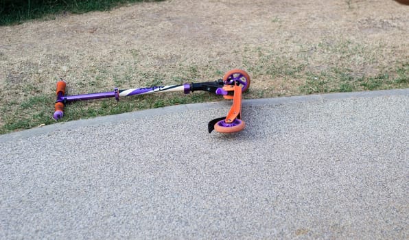 A child 's scooter thrown on the ground lies on the playground . Sports equipment. Outdoor games. Sport. Entertainments.