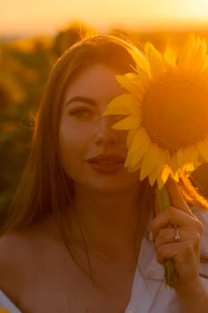 A girl in a hat on a beautiful field of sunflowers against the sky in the evening light of a summer sunset. Sunbeams through the flower field. Natural background