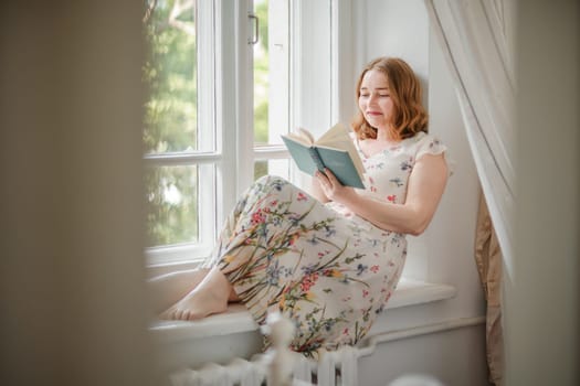 A middle-aged woman in a cream dress sits mysteriously and looks out the window on the windowsill. Green trees outside