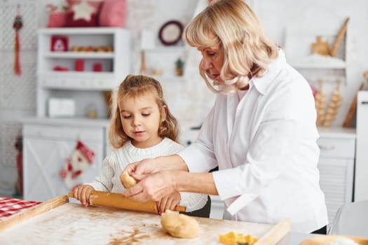 Senior grandmother with her little granddaughter cooks sweets for Christmas on the kitchen.