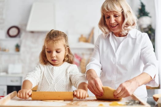 Kneads the dough. Senior grandmother with her little granddaughter cooks sweets for Christmas on the kitchen.