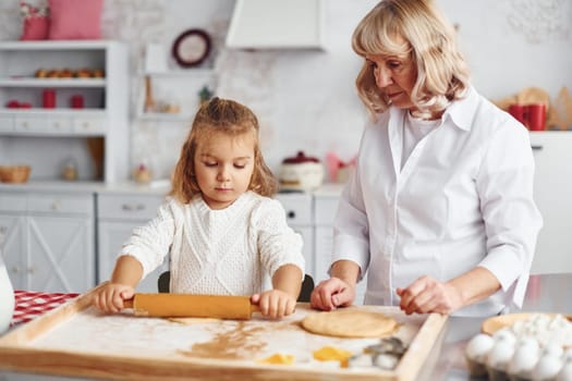 Kneads the dough. Senior grandmother with her little granddaughter cooks sweets for Christmas on the kitchen.