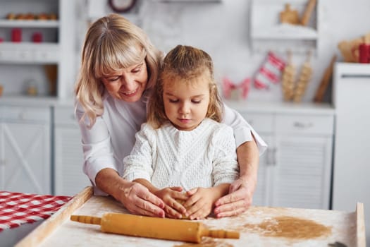 Kneads the dough. Senior grandmother with her little granddaughter cooks sweets for Christmas on the kitchen.