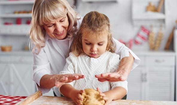 Kneads the dough. Senior grandmother with her little granddaughter cooks sweets for Christmas on the kitchen.