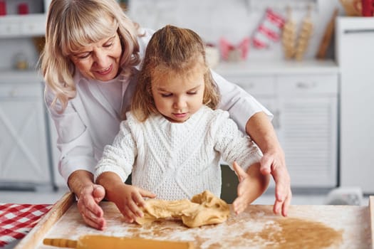 Kneads the dough. Senior grandmother with her little granddaughter cooks sweets for Christmas on the kitchen.
