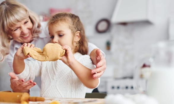 Kneads the dough. Senior grandmother with her little granddaughter cooks sweets for Christmas on the kitchen.
