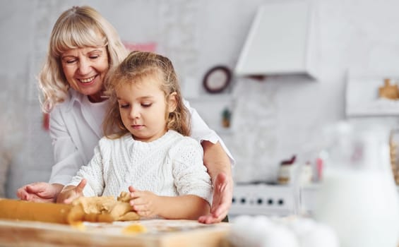 Kneads the dough. Senior grandmother with her little granddaughter cooks sweets for Christmas on the kitchen.