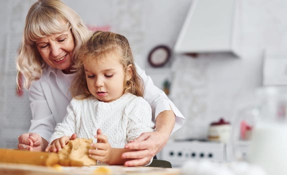 Kneads the dough. Senior grandmother with her little granddaughter cooks sweets for Christmas on the kitchen.