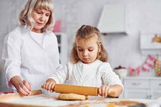 Kneads the dough. Senior grandmother with her little granddaughter cooks sweets for Christmas on the kitchen.