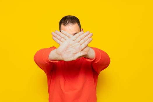 Hispanic man standing over yellow background rejection expression crossing his arms and palms covering his face making a negative sign