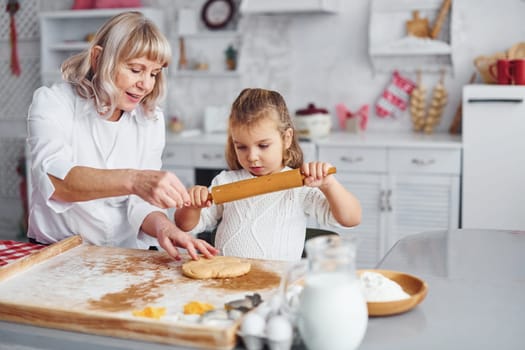 Senior grandmother with her little granddaughter cooks sweets for Christmas on the kitchen.