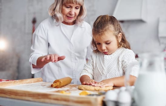 Senior grandmother with her little granddaughter cooks sweets for Christmas on the kitchen.