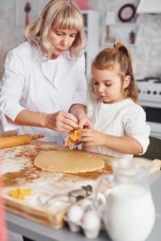 Senior grandmother with her little granddaughter cooks sweets for Christmas on the kitchen.