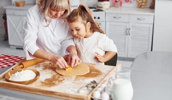 Senior grandmother with her little granddaughter cooks sweets for Christmas on the kitchen.