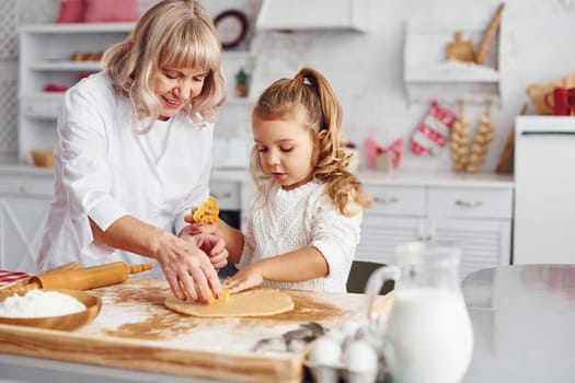 Senior grandmother with her little granddaughter cooks sweets for Christmas on the kitchen.
