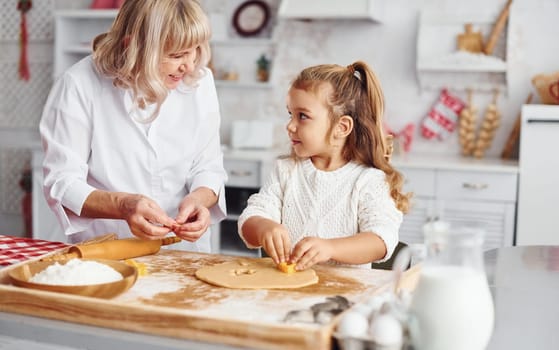 Senior grandmother with her little granddaughter cooks sweets for Christmas on the kitchen.
