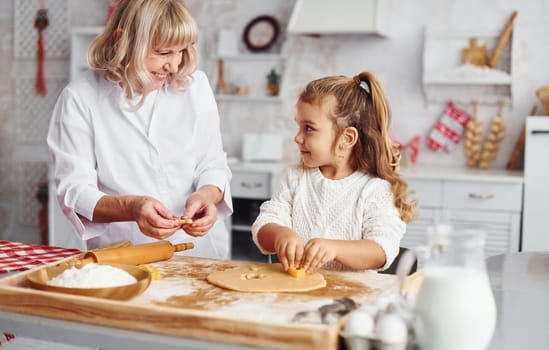Senior grandmother with her little granddaughter cooks sweets for Christmas on the kitchen.