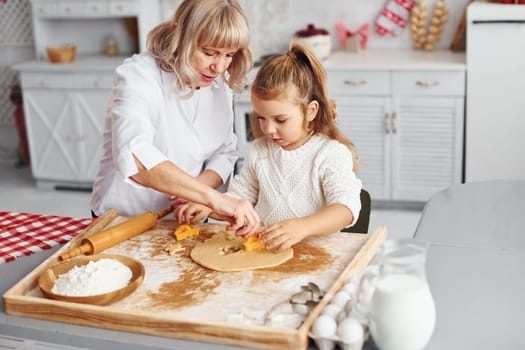 Senior grandmother with her little granddaughter cooks sweets for Christmas on the kitchen.