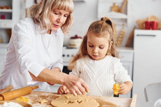 Senior grandmother with her little granddaughter cooks sweets for Christmas on the kitchen.