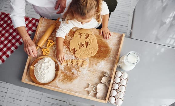 Top view of senior grandmother that with her little granddaughter cooks sweets for Christmas on the kitchen.