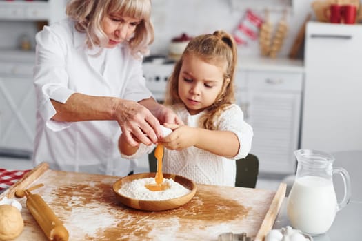 Uses eggs. Senior grandmother with her little granddaughter cooks sweets for Christmas on the kitchen.