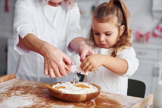 Uses eggs. Senior grandmother with her little granddaughter cooks sweets for Christmas on the kitchen.