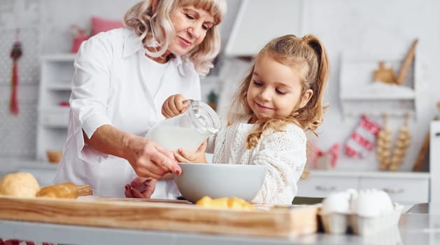 Fills with milk. Senior grandmother with her little granddaughter cooks sweets for Christmas on the kitchen.
