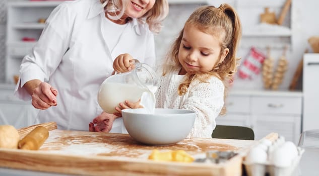 Fills with milk. Senior grandmother with her little granddaughter cooks sweets for Christmas on the kitchen.