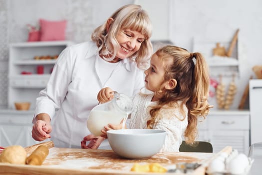 Fills with milk. Senior grandmother with her little granddaughter cooks sweets for Christmas on the kitchen.
