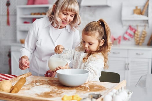Fills with milk. Senior grandmother with her little granddaughter cooks sweets for Christmas on the kitchen.