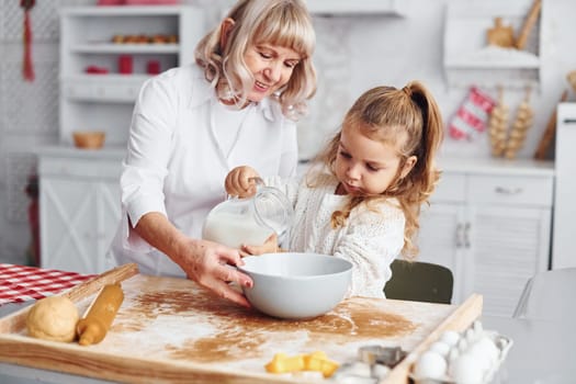 Fills with milk. Senior grandmother with her little granddaughter cooks sweets for Christmas on the kitchen.