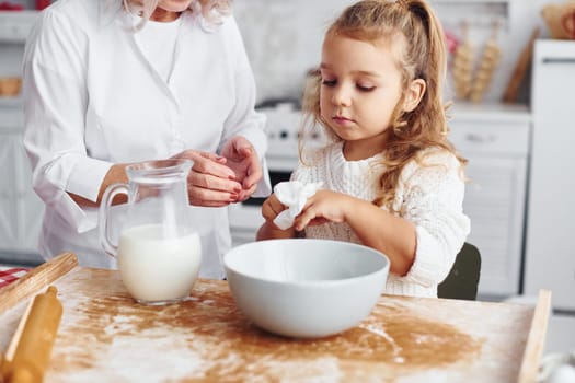 Fills with milk. Senior grandmother with her little granddaughter cooks sweets for Christmas on the kitchen.