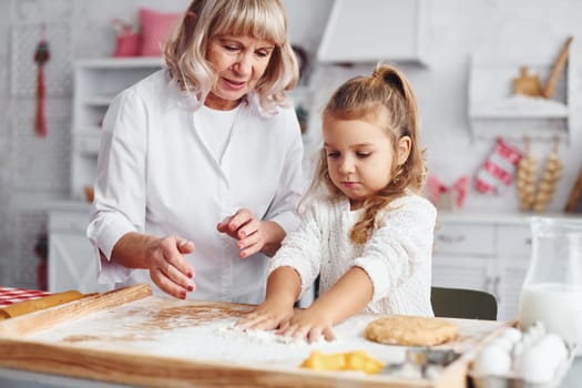 Teaching process. Senior grandmother with her little granddaughter cooks sweets for Christmas on the kitchen.
