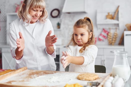 Teaching process. Senior grandmother with her little granddaughter cooks sweets for Christmas on the kitchen.