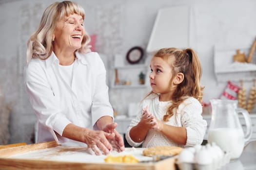 Teaching process. Senior grandmother with her little granddaughter cooks sweets for Christmas on the kitchen.