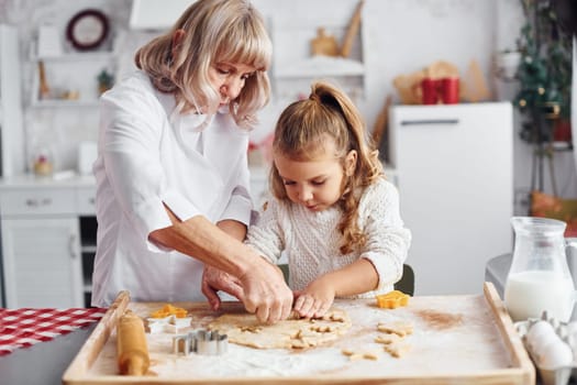 Teaching process. Senior grandmother with her little granddaughter cooks sweets for Christmas on the kitchen.