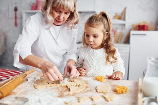 Teaching process. Senior grandmother with her little granddaughter cooks sweets for Christmas on the kitchen.