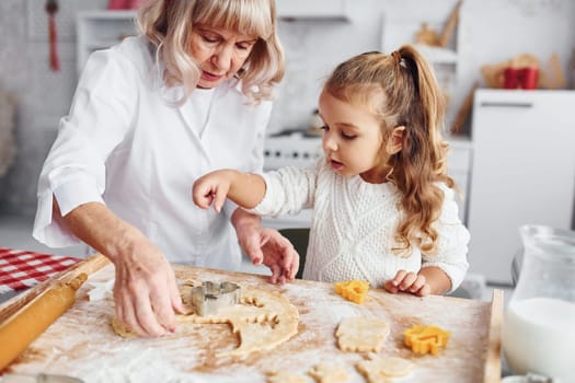 Teaching process. Senior grandmother with her little granddaughter cooks sweets for Christmas on the kitchen.