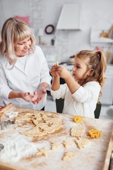 Teaching process. Senior grandmother with her little granddaughter cooks sweets for Christmas on the kitchen.