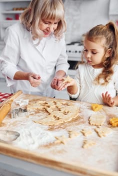 Teaching process. Senior grandmother with her little granddaughter cooks sweets for Christmas on the kitchen.