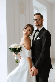 groom in a black suit with a bow tie and the bride in a tight white dress in a bright studio