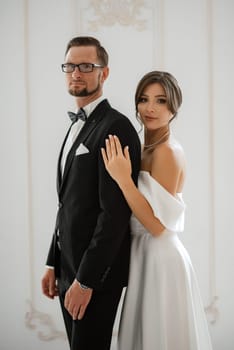 groom in a black suit with a bow tie and the bride in a tight white dress in a bright studio