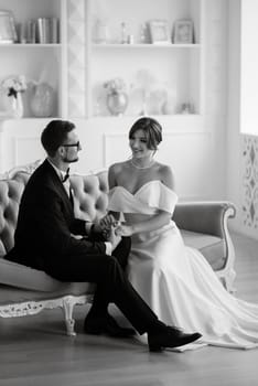 groom in a black suit with a bow tie and the bride in a tight white dress in a bright studio