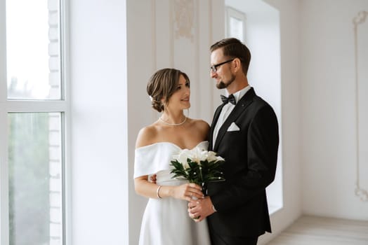 groom in a black suit with a bow tie and the bride in a tight white dress in a bright studio