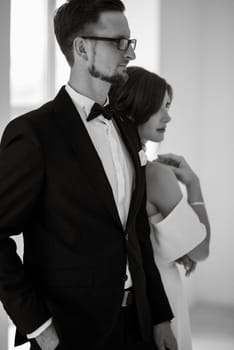 groom in a black suit with a bow tie and the bride in a tight white dress in a bright studio