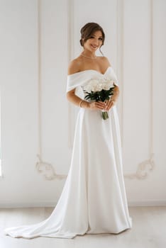 brunette bride in a tight wedding dress in a bright studio with a bouquet