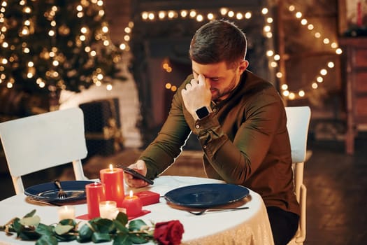 Young handsome man sits by the table and waits for girlfriend for romantic dinner in restaurant.