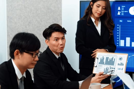 Confidence and young asian businesswoman give presentation on financial business strategy in dashboard report display on screen to colleagues in conference room meeting as harmony in workplace concept