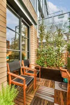 two chairs on a wooden deck with plants in the foreground and an open door leading to a balcony area