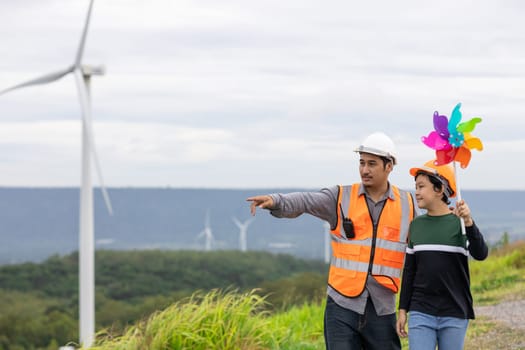 Engineer with his son holding windmill toy on a wind farm atop a hill or mountain. Progressive ideal for the future production of renewable, sustainable energy. Energy generated from wind turbine.